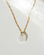 Gold necklace with a white moonstone pendant on a white background