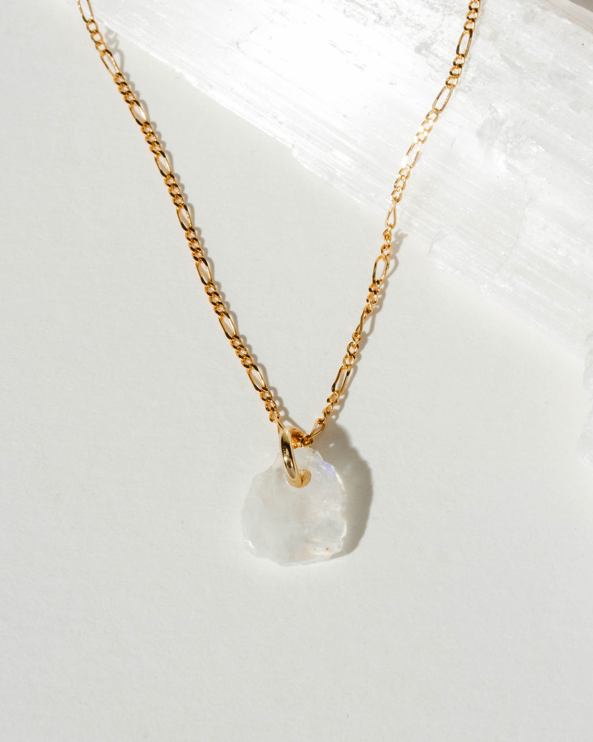 Gold necklace with a white moonstone pendant on a white background