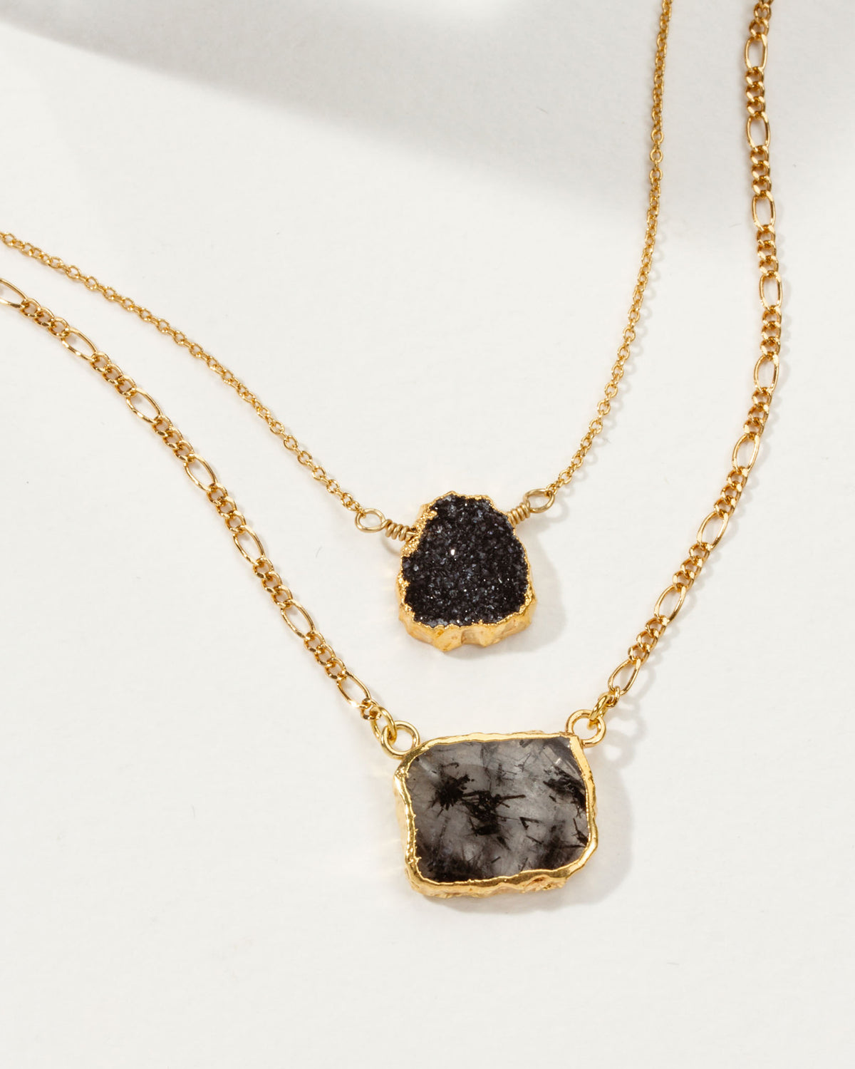 Two-tiered gold chain necklace with black druzy crystal and black-on-white stone pendants.
