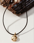 A gold disc pendant necklace on a thin black cord.