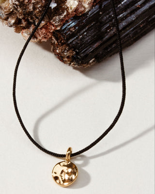 A gold disc pendant necklace on a thin black cord.
