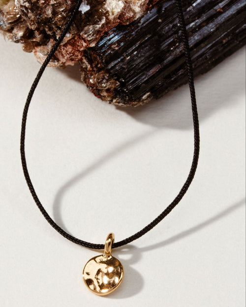 A gold disc pendant necklace on a thin black cord.