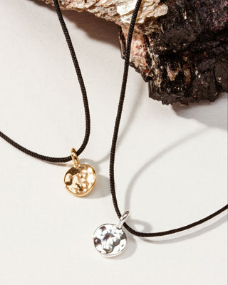 Two delicate cord necklaces with small round hammered pendants, one gold-toned and one silver-toned.