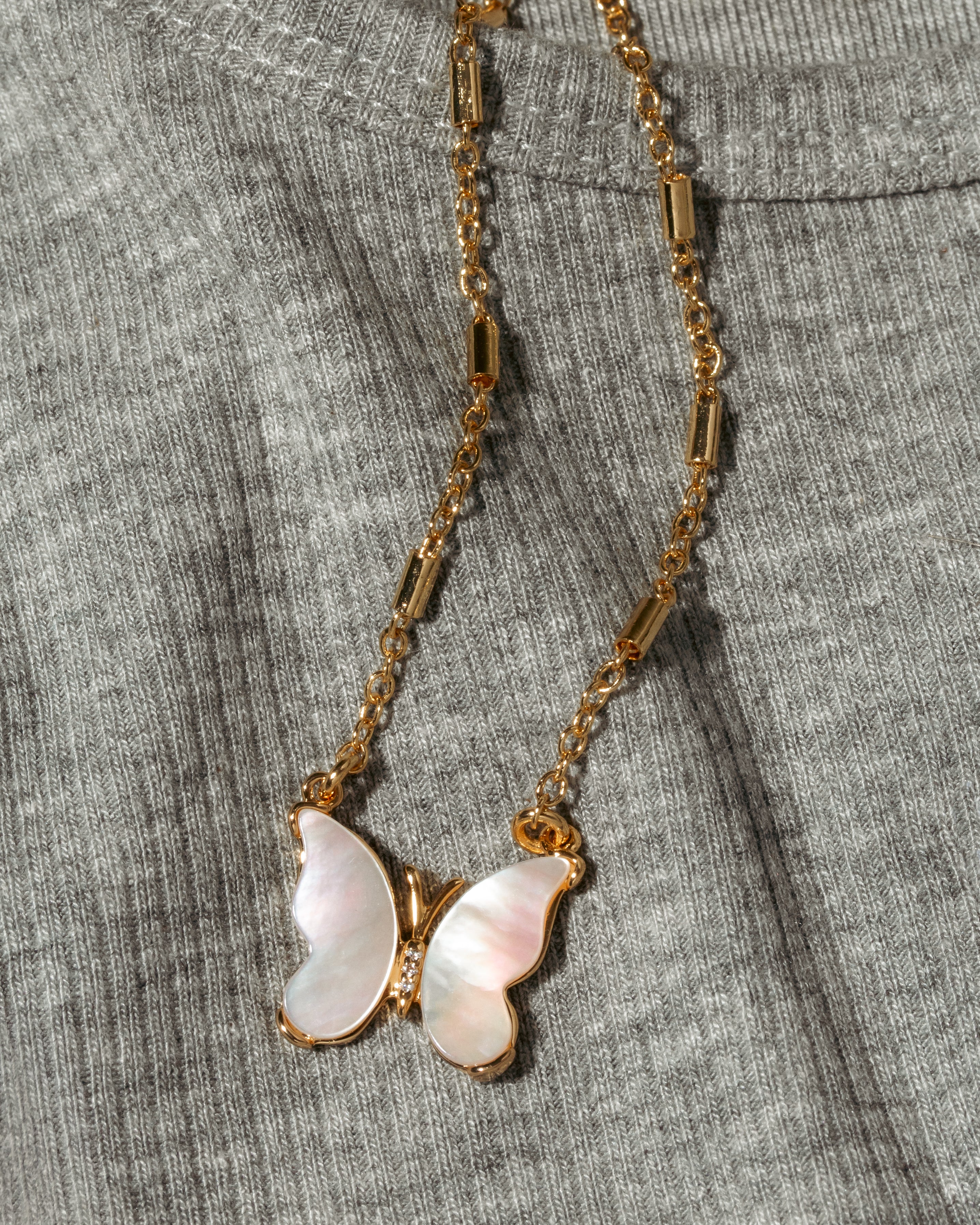 A gold chain necklace with a butterfly pendant made of iridescent mother-of-pearl wings.