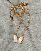 A gold-tone necklace with a mother-of-pearl butterfly pendant, laid flat on a textured gray knit garment.