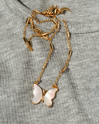 A gold-tone necklace with a mother-of-pearl butterfly pendant, laid flat on a textured gray knit garment.
