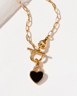 Gold chain necklace with a toggle clasp and a heart-shaped padlock pendant featuring a black onyx center.