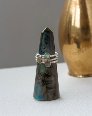 Three silver rings, each with turquoise, labradorite gemstones displayed on a greenish crystal tower.