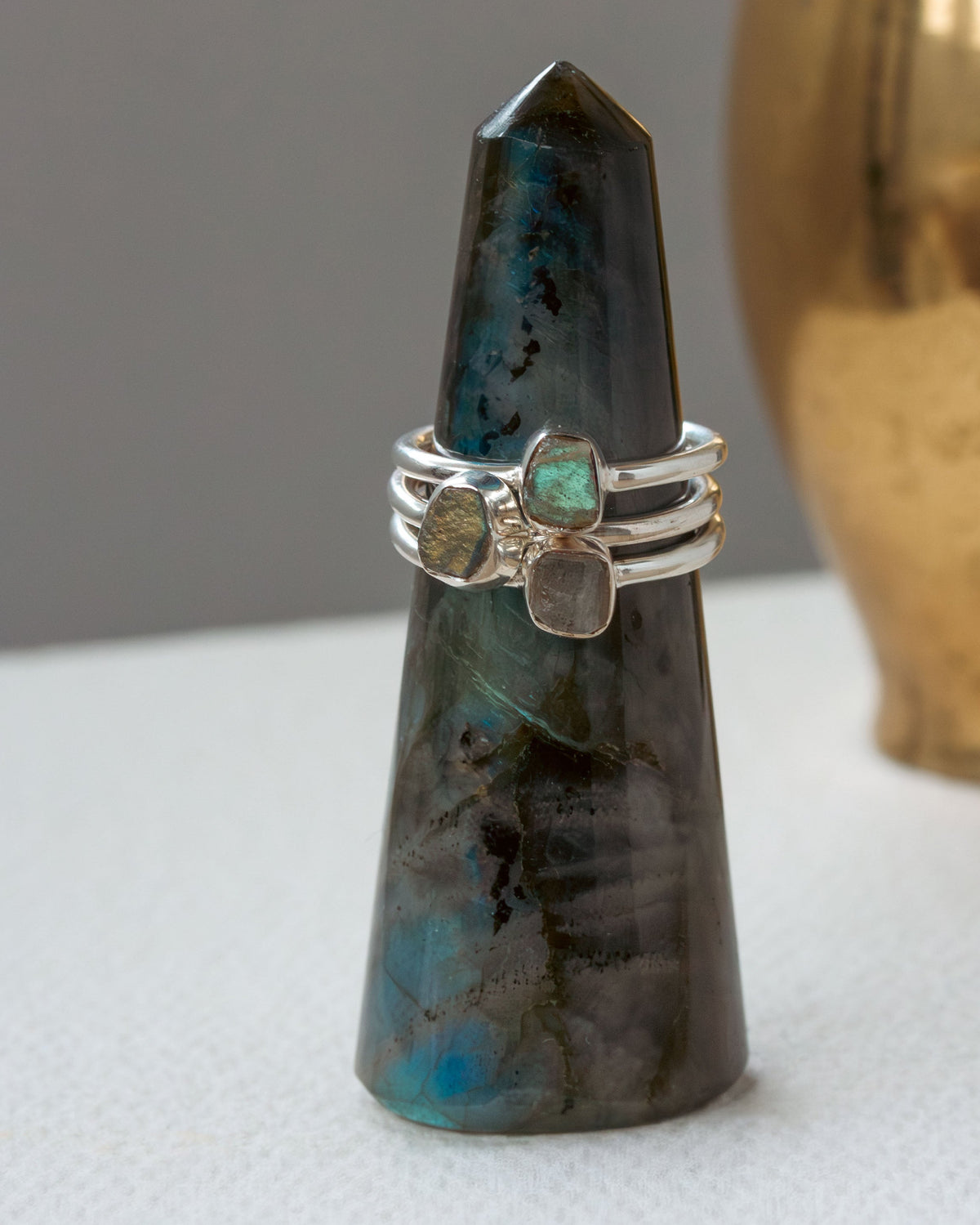 Three silver rings, each with turquoise, labradorite gemstones on a greenish crystal tower.
