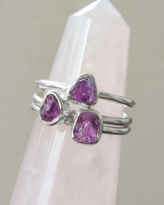 Closeup of three silver rings, each with purple amethyst gemstones on a white crystal tower.