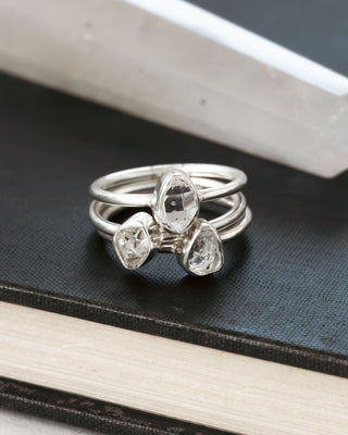 Three stacking silver rings, one ontop of each other, with teardrop-shaped herkimer quartz gemstones on a black surface