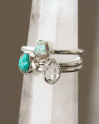 Three silver rings with turquoise, labradorite, and Herkimer quartz gems on a white crystal tower.