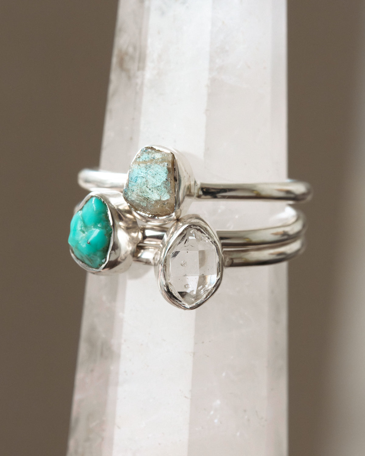 Three silver rings with turquoise, labradorite, and Herkimer quartz gems on a white crystal tower.