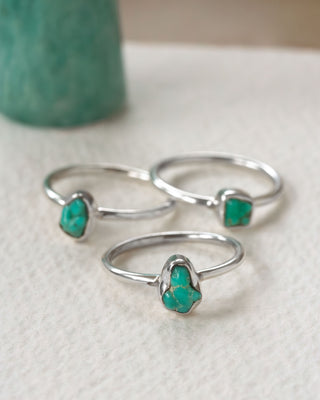 Three silver rings, each with turquoise gemstones displayed on a white surface.