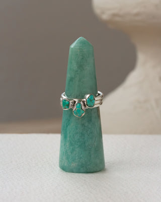 Three silver rings, each with turquoise gemstones displayed on green crystal tower.