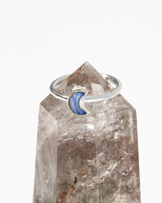 A silver ring featuring a crescent moon inlay with labradorite genuine stone, displayed on a quartz crystal point.
