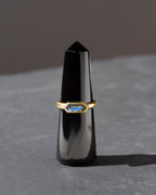 Gold ring with a blue gemstone on a black stand against a gray background