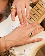 Close-up of hands playing a guitar with gold rings and bracelets.