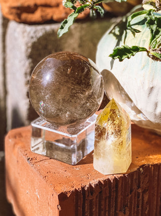 Crystal ball and crystal on a wooden surface with plants in the background
