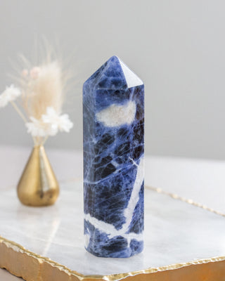 Blue and white marbled  sodalite crystal tower on a marble surface with a gold base.