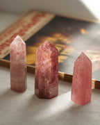 Three pink strawberry quartz crystal towers on a textured surface with a book in the background