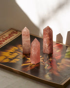 Three strawberry quartz crystal towers standing on a vintage book casting shadows from intense light