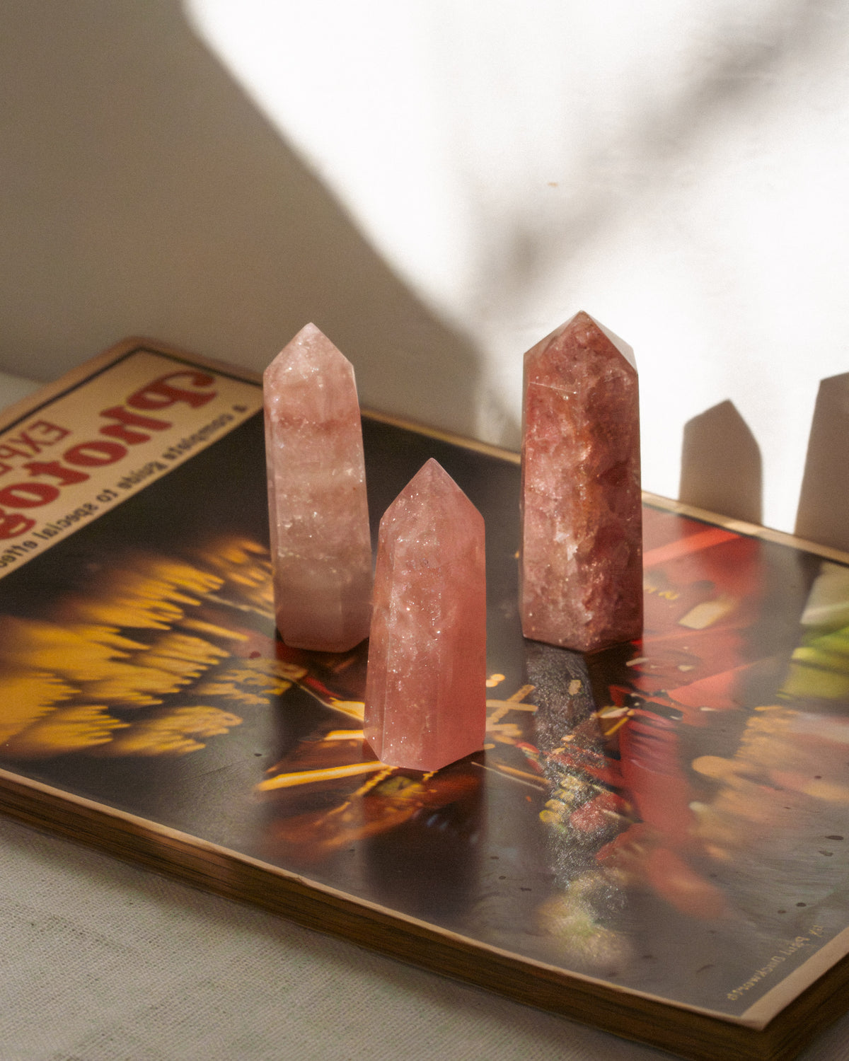 Three strawberry quartz crystal towers standing on a vintage book casting shadows from intense light