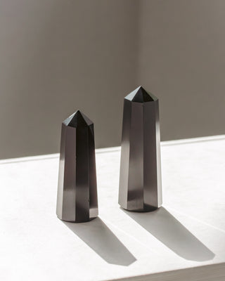 Two black onyx, pyramid obelisk-shaped objects on a reflective surface with a neutral background