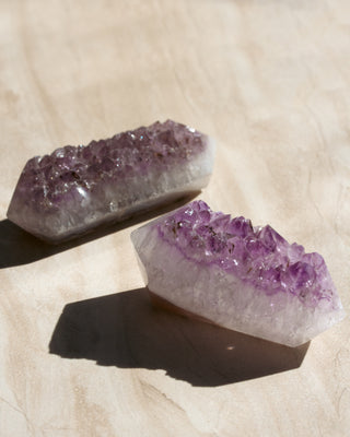 Two amethyst crystal formations on a beige surface