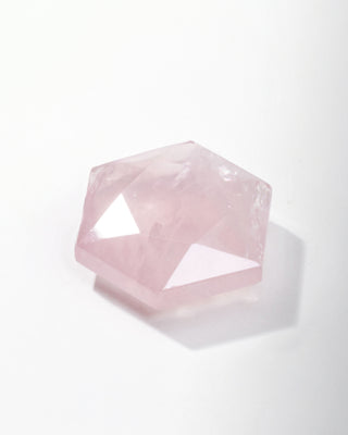Pink facetted geometric rose quartz crystal on a white background