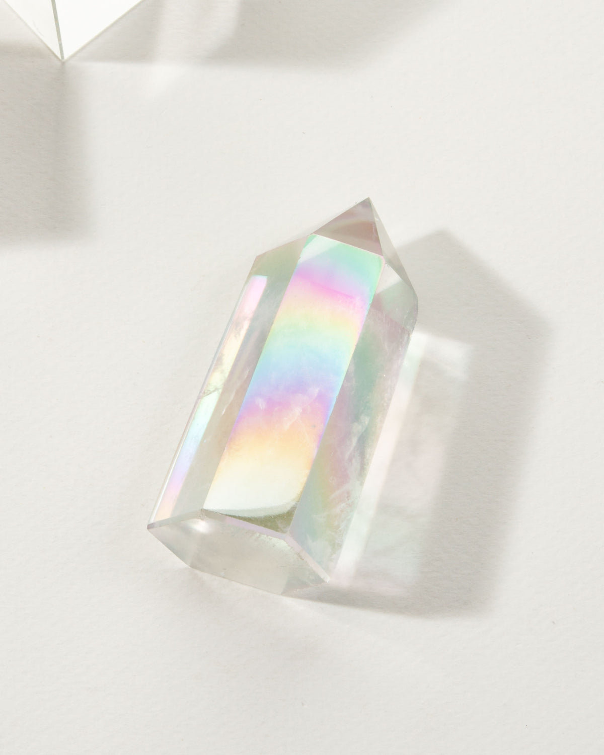 Aura Quartz crystal tower with rainbow iridescence is on a white surface.