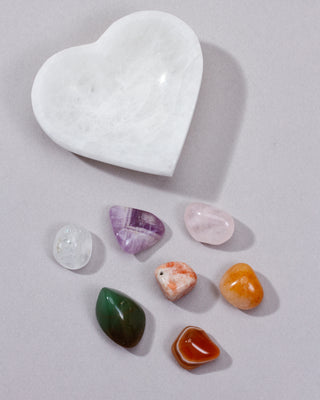 Heart-shaped white stone with various colorful crystals on a light gray background