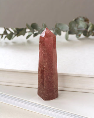 Pink crystal obelisk on a white surface with greenery in the background
