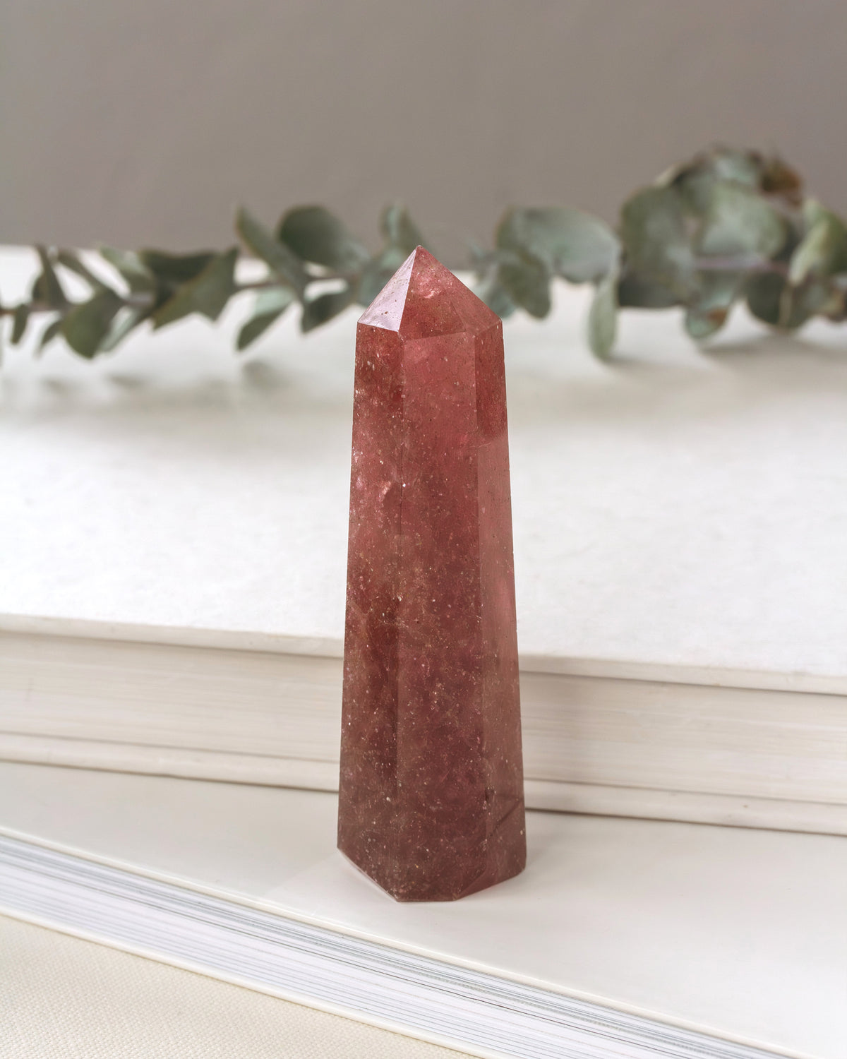 Pink crystal obelisk on a white surface with greenery in the background