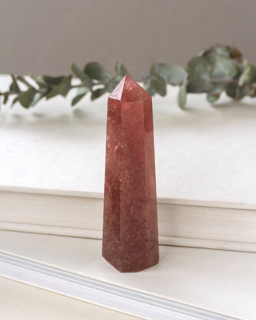 Pink crystal obelisk on a white surface with greenery in the background