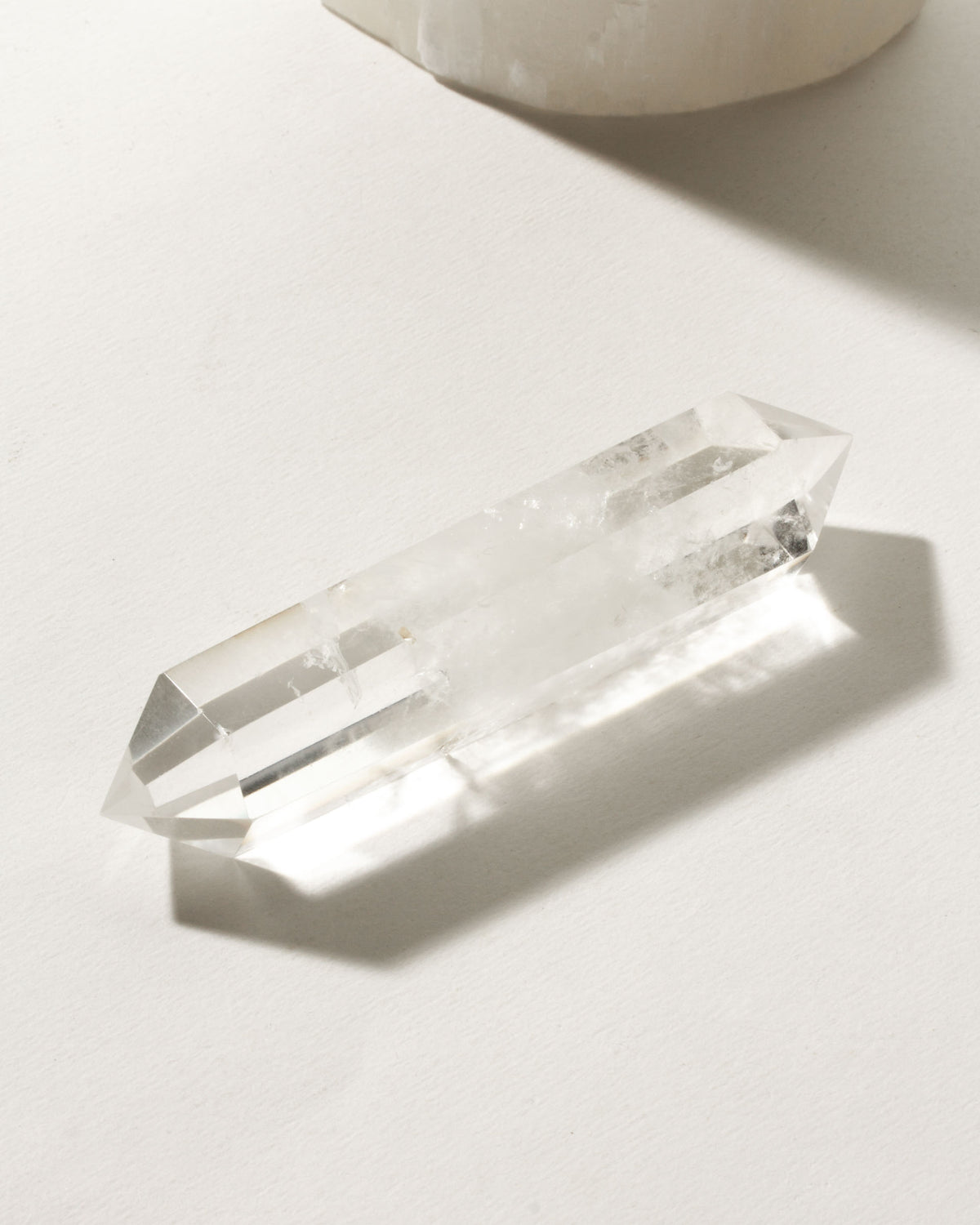 Clear quartz Krystallos double point wand on a white surface.