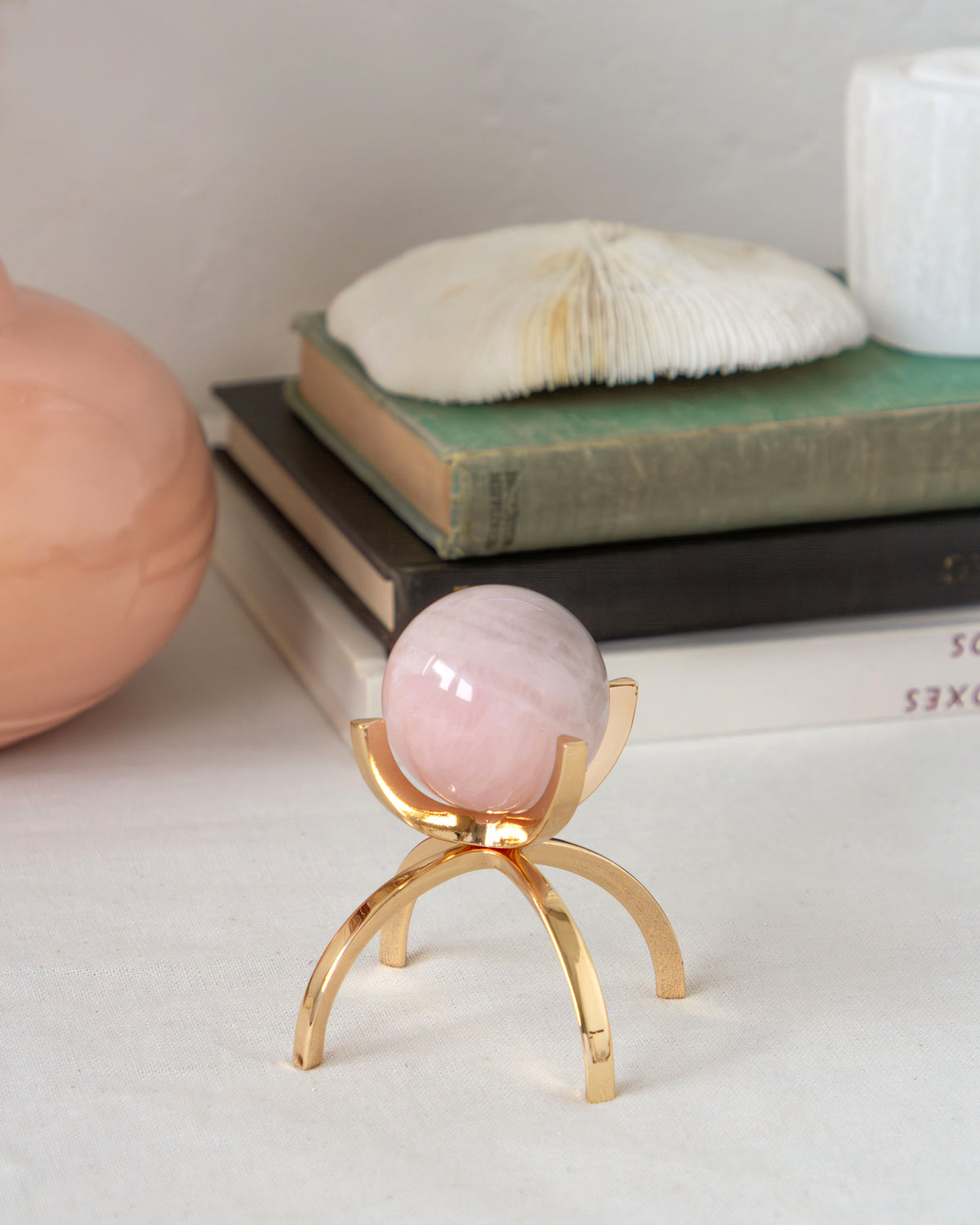 Pink rose quartz crystal ball on a gold stand with decorative items in the background