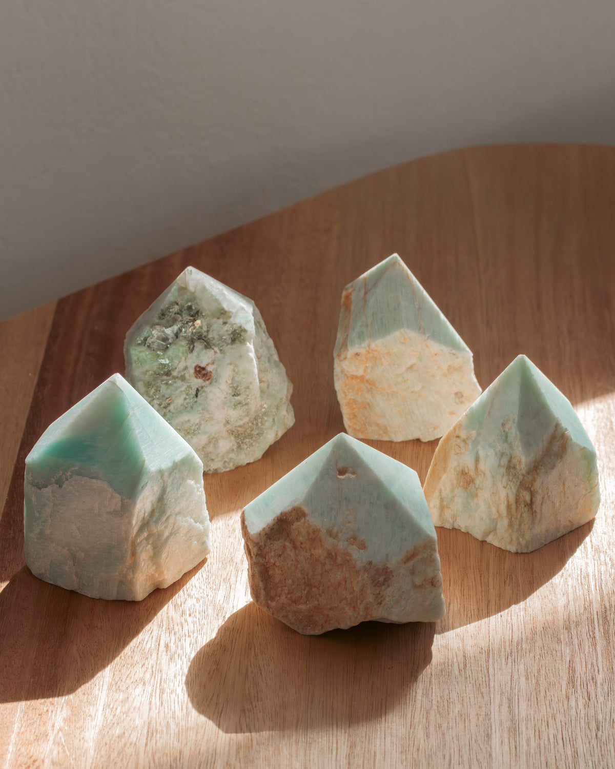 Five green and beige crystal-like stones on a wooden surface