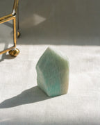 Green crystal on a white surface with a gold object in the background