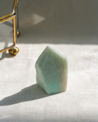 Green crystal on a white surface with a gold object in the background