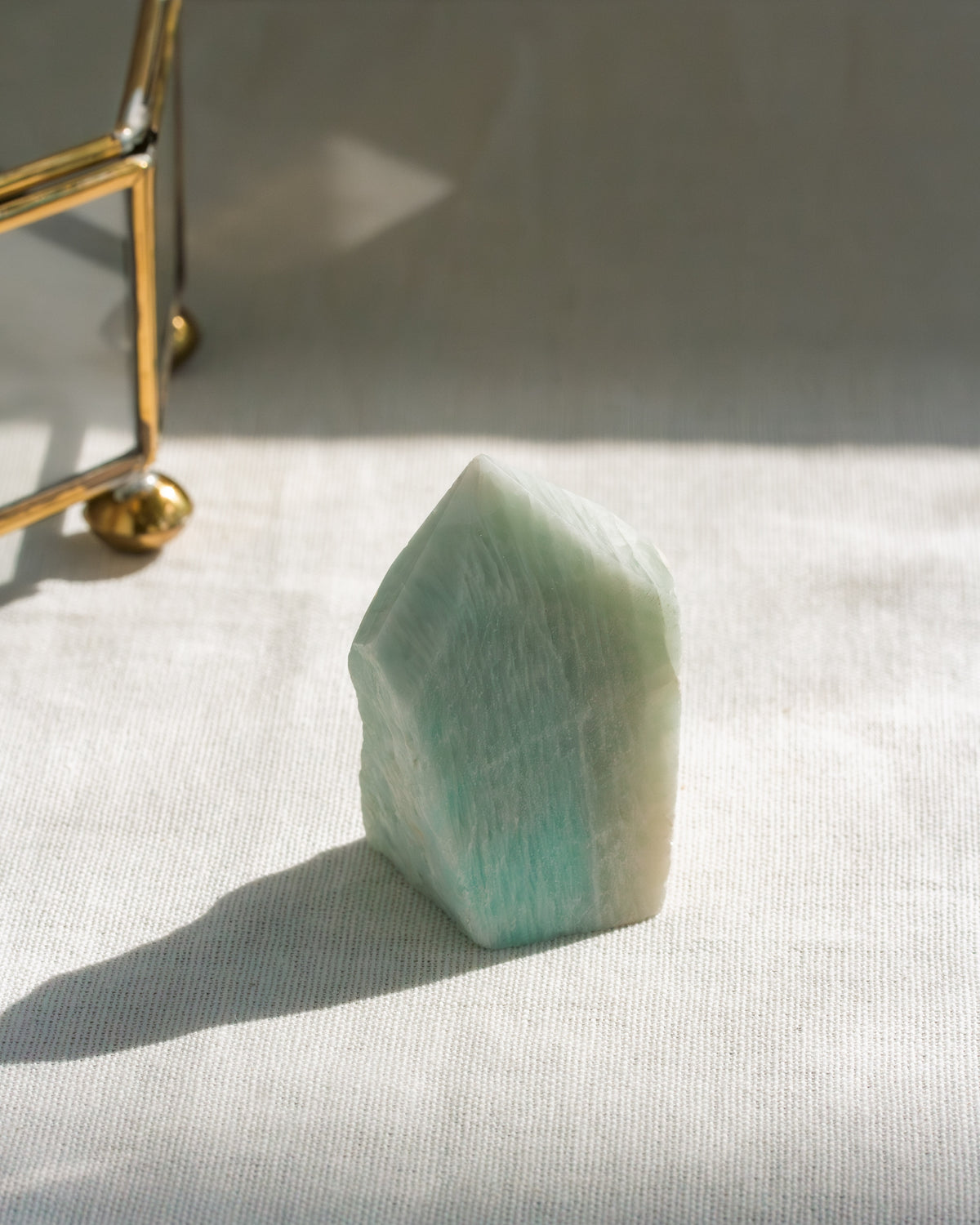 Green crystal on a white surface with a gold object in the background