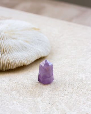 Purple crystal on a beige surface with a shell in the background