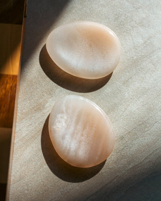 Two smooth beige Peach Aventurine stones on a textured surface