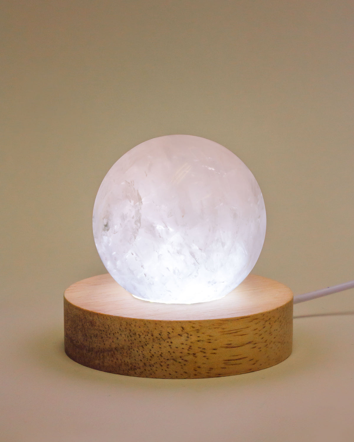 Rose quartz sphere lamp on a wooden base, illuminated with a USB cord.