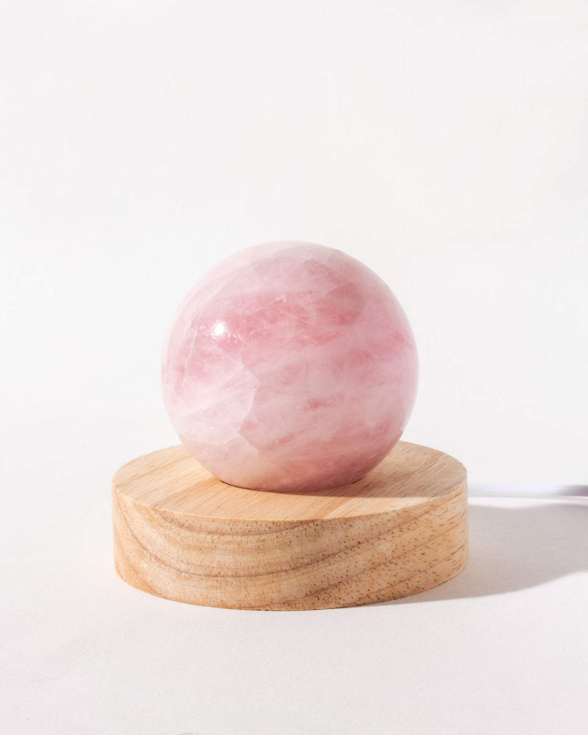 Rose quartz sphere atop a wooden base, designed as a travel lamp.