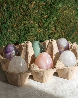 Colorful crystal eggs in a cardboard egg carton against a green foliage background