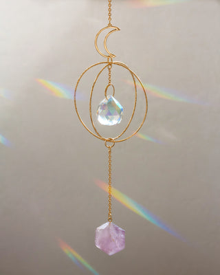 Decorative hanging crystal with gold chain and rainbow effect on a neutral background