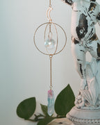 Decorative hanging crystal with gold chain on a white surface with green leaves in the background