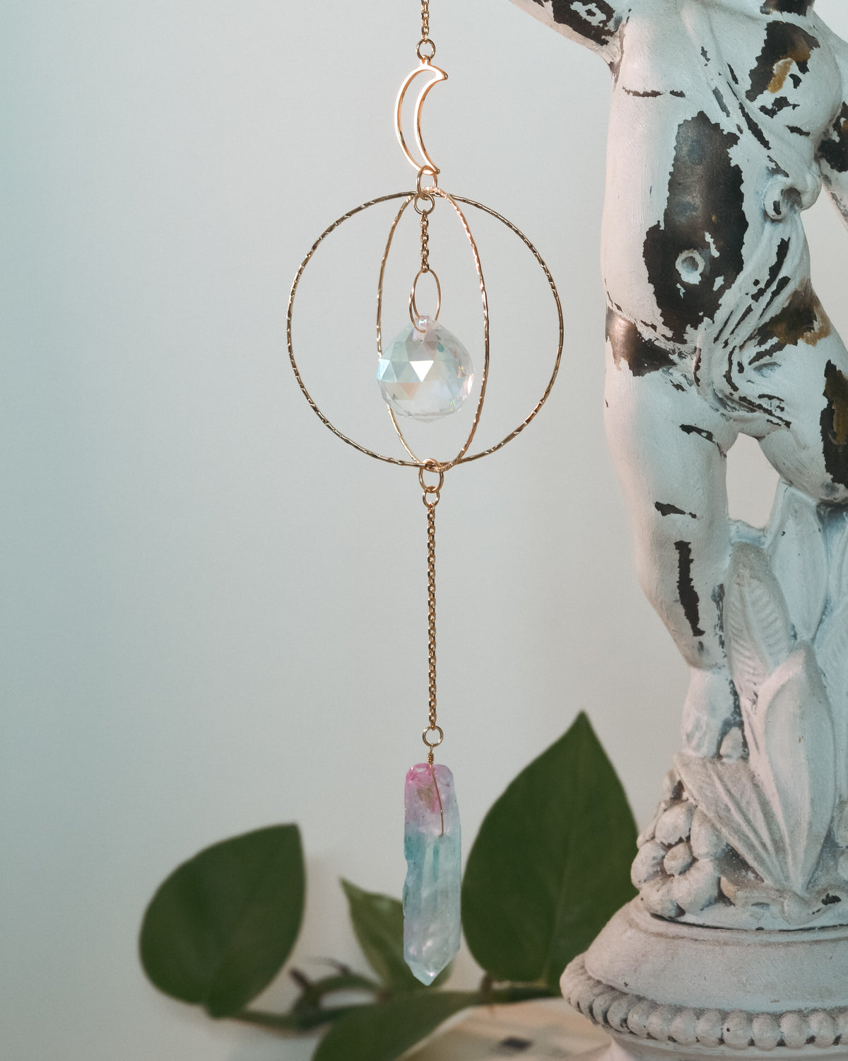 Decorative hanging crystal with gold chain on a white surface with green leaves in the background
