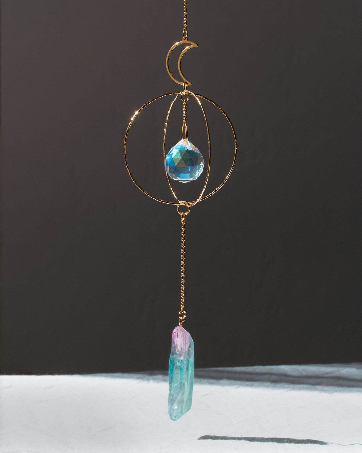 Decorative hanging crystal with gold chain and blue crystal on a dark background